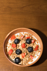 Fresh corn flakes cereal and fruits strawberry and blueberry in wood bowl