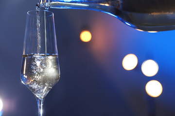 Champagne pouring from bottle into glass on color background, closeup. Space for text