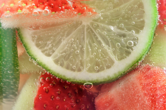 Refreshing fruit sparkling water from strawberries and lime in a glass mug close-up, background.