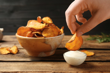Woman dipping sweet potato chip into sauce on table, closeup