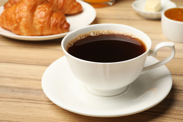 Cup of tasty aromatic coffee and croissants for breakfast on wooden table