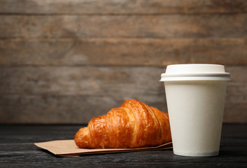 Paper cup with coffee and croissant on wooden table. Mockup for design