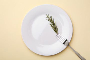 Plate with rosemary and fork on color background, flat lay