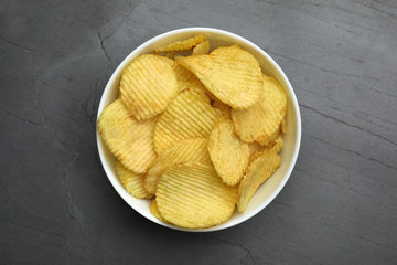 Bowl of potato chips on grey table, top view