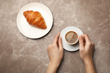 Woman with cup of coffee and croissant on color background, flat lay