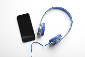 Stylish headphones and modern phone on white background, top view. Space for text