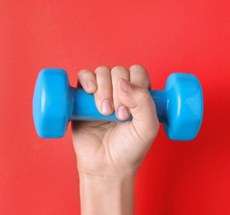 Woman holding vinyl dumbbell on color background, closeup