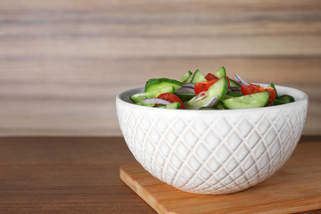 Bowl of tasty cucumber tomato salad on wooden table. Space for text