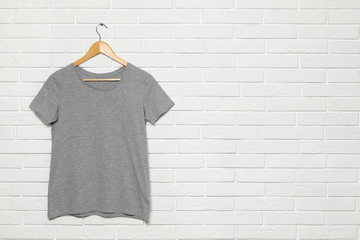 Hanger with blank t-shirt on white brick wall. Mock up for design