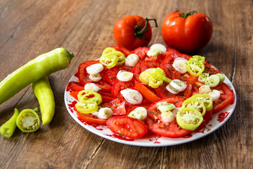 Salad with fresh tomatoes, young onion and hot paprika on wooden table