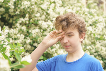 Naklejka na ściany i meble Teenager with allergies standing in a blue t-shirt among the Jasmine bushes and suffers from bad health
