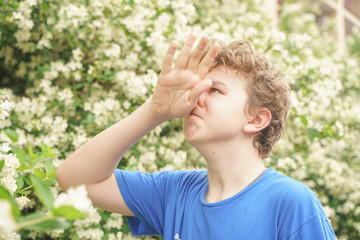 Teenager with allergies standing in a blue t-shirt among the Jasmine bushes and suffers from bad health
