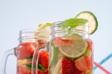 Two mugs with fruit refreshing water from strawberries, lemon, mint and lime in the background of drinking tubes.