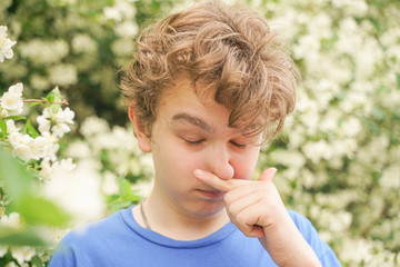 Teenager with allergies standing in a blue t-shirt among the Jasmine bushes and suffers from bad health