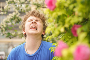 Teenager with allergies standing in a blue t-shirt among the Jasmine bushes and suffers from bad health