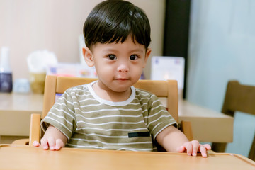 Portrait Of Happy Young Baby Boy In High Chair. Child sitting at empty table.Baby nutrition concept.Food advertisement design. smiling baby sitting on baby Chair.