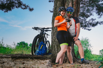 Naklejka na ściany i meble Happy couple searching on map in smartphone destination. man and woman in helmets traveling mountain biking over rough terrain. Theme tourism and navigation, search way, create route, gps phone app