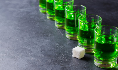 Absinthe green liquor in glasses. Alcoholic hallucinogenic beverage. Dark background. Pieces of...