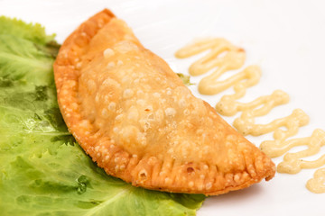 Traditional cheburek pie (meat in dough fried in hot oil) on plate with sauce and salad leaf