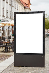 Vertical shot of blank billboard stands on pavemenet against city background near outdoor cafeteria, copy space area for your text message, public information or promotional content. Street poster