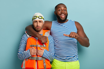 Glad dark skinned guy embraces sorrowful companion, says look at this guy who cannot swim, have fun...