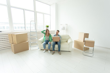 Cheerful joyful young couple charming girl and handsome man holding a box with things and a pot with a plant while moving to a new apartment.