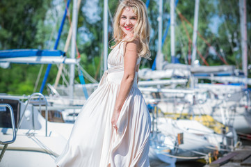 Fototapeta premium Nice blonde lady in yacht club. Woman in flying silk white dress at outdoor, relax time