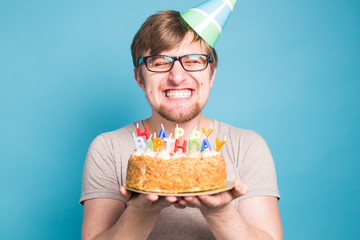 Crazy funny young man in glasses and paper congratulatory hats holding cakes happy birthday standing on a blue background.