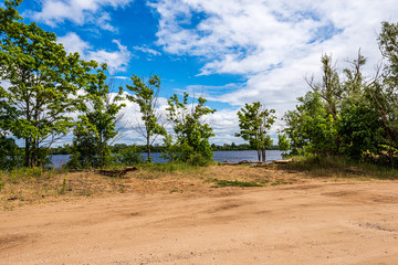 Fototapeta premium spring by the lake with green foliage grass in meadow and blue water