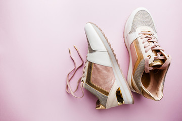 Fashion blog look. White women's sneakers with pink and gold color on pink background. Flat lay, top view beauty female background.