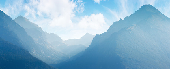 panorama of mountain ridge. bright scenery in afternoon hazy light. sky with fluffy clouds. valley between ridges. beautiful landscape backdrop