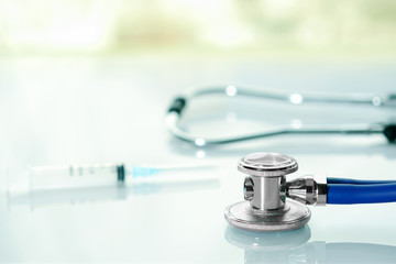 Stethoscope or phonendoscope on a doctor's white desk near window with syringe. Treatment of cold...