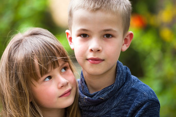 Two cute fair-haired children siblings, young boy brother and sister girl outdoors on bright sunny green bokeh background. Family relation, friendship and love concept.