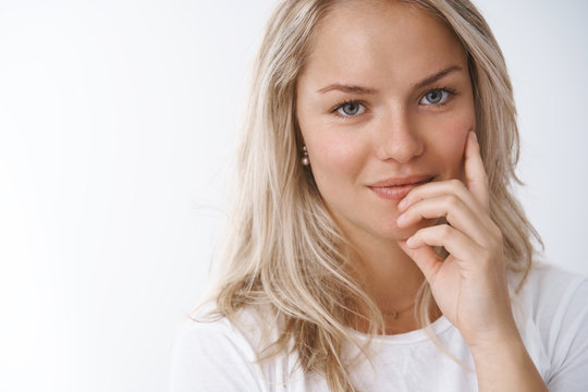 Headshot of tender and sensual attractive european blonde in white t-shirt seducting touching lip flirty and smiling cheeky at camera posing feminine against white background