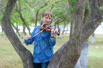 The young Russian woman with a violin costs at a tree in the park in the summer