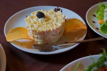 Studio Photo . Salad with fried potato pie on a white plate, selective focus . Potato Mayonnaise salad .Salty chips for an aperitif in close-up . Portion layered salad with fish, carrots and eggs.