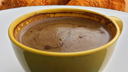 A cup of morning coffee. A cup of coffee served with breakfast. Roll with sesame in the background.