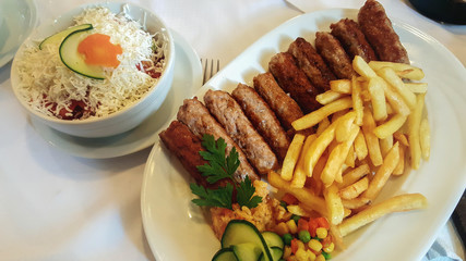 A serving of kebabs with fried potatoes and vegetables in a plate. Chicken salad, vegetables and cheese.