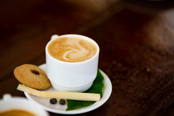 A cup of hot coffee on white plate with cake, peace of cane and leaves. Placed on old bar counter. Cuba, space for text