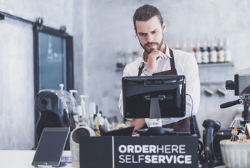 Confident young barista young man looking for a digital equipment to pay for the business. The...