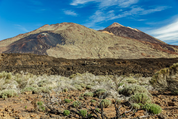 Mountain Teide with white snow spots, partly covered by the clouds. Bright blue sky. Teide National Park, Tenerife, Canary Islands, Spain.