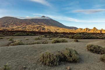 Mountain Teide with white snow spots, partly covered by the clouds. Bright blue sky. Teide National Park, Tenerife, Canary Islands, Spain.