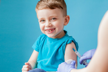 Vaccination concept. Female doctor vaccinating cute little boy on blue background, closeup