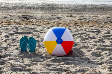 Flip flops on beach sand with colorful beach ball