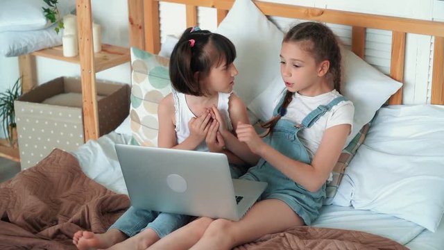 Little girls watch something on laptop and emotionally discuss it, slow motion