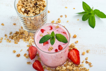 A glass of healthy strawberry yogurt with fresh berries, muesli and mint on a white wooden table. Healthy breakfast.