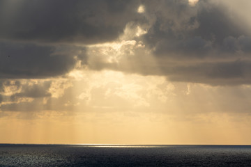 Obraz premium Dramatic sunset over sea water with gray clouds and sun lights