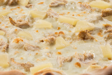 Pizza topped with sauce, chicken, cheese and pineapple serve on wooden plate on wooden table. Photo of Hawaiian pizza. 