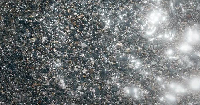 4K footage of some rocks under water, in a lake shore, with small waves and sunlight.