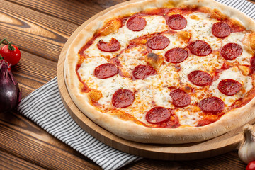 Delicious hot homemade Pepperoni pizza on the wooden table. Pepperoni Pizza - Fresh homemade pizza with pepperoni, cheese and tomato sauce on rustic black stone background wirh copy space.  